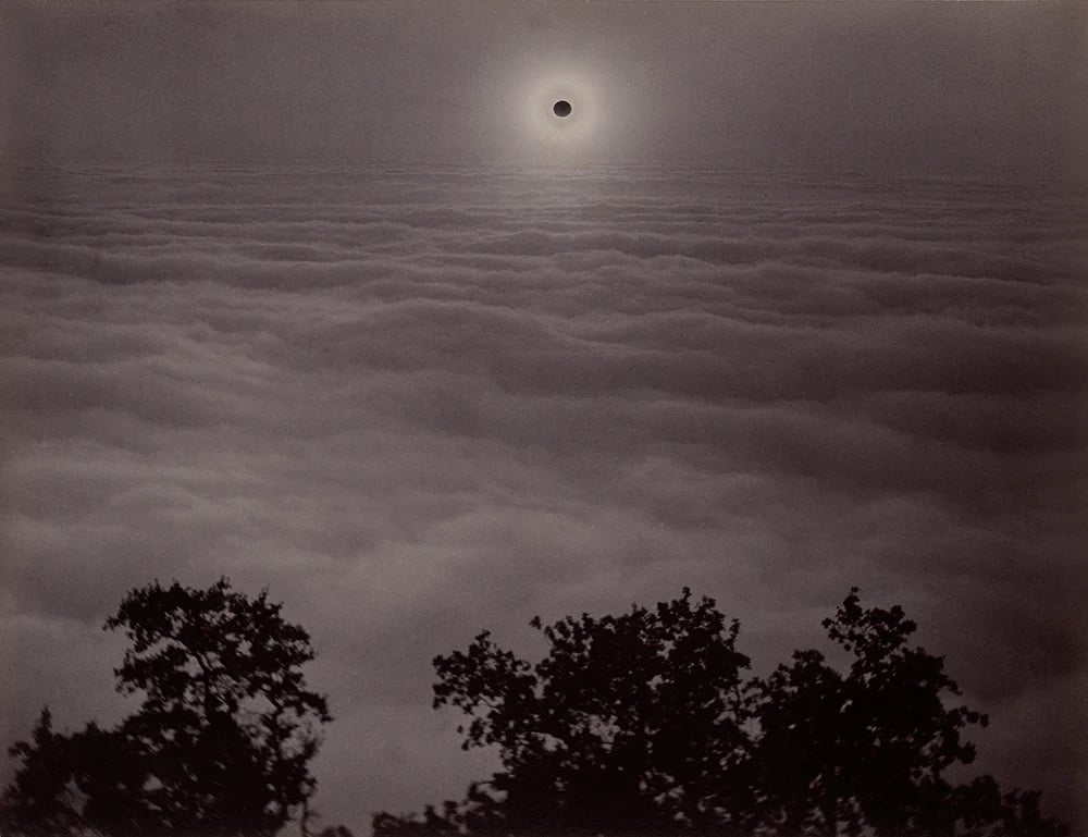 photo of a solar eclipse over a bank of clouds