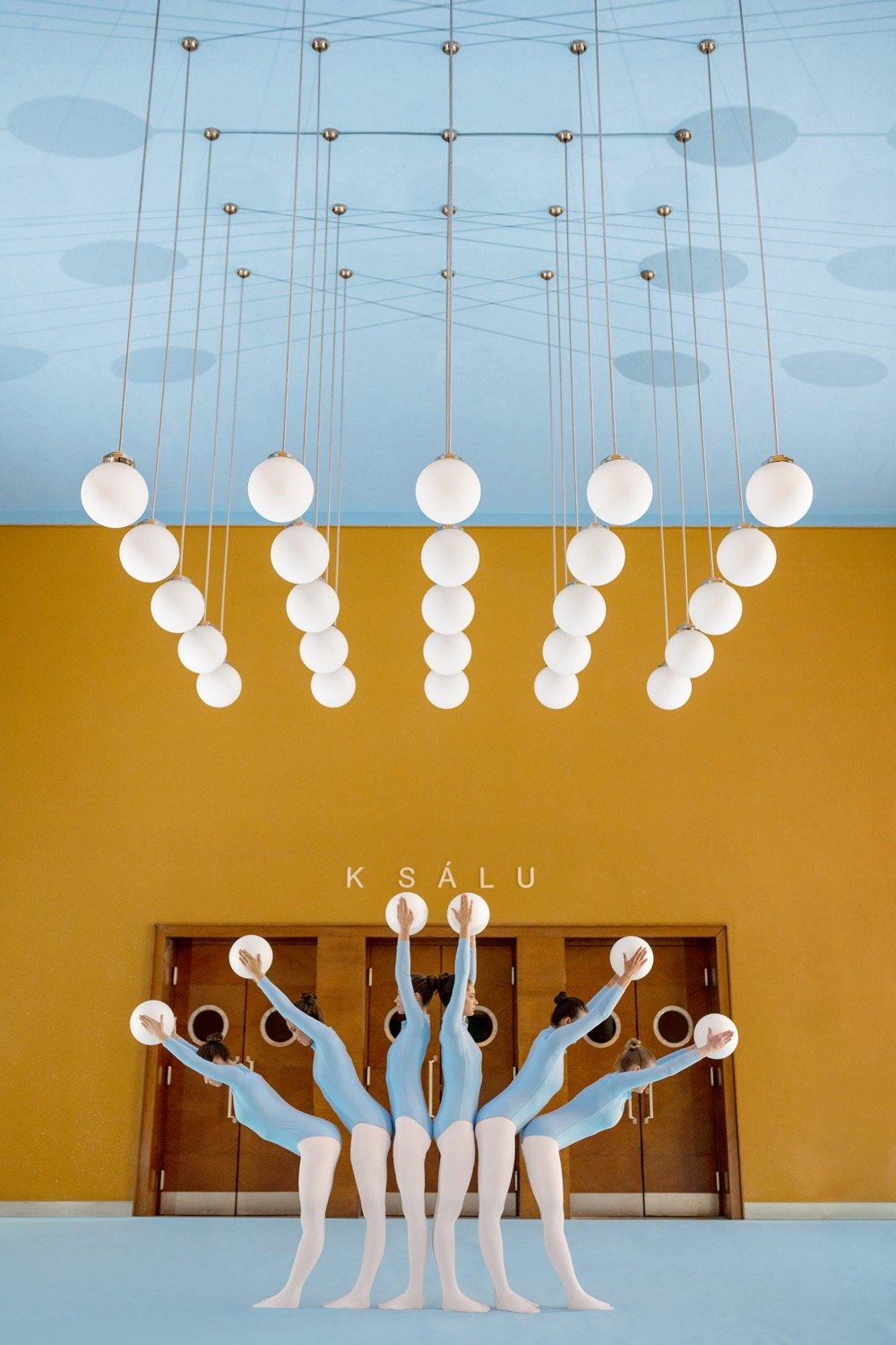 five women holding white balls that mirror the light fixtures above them
