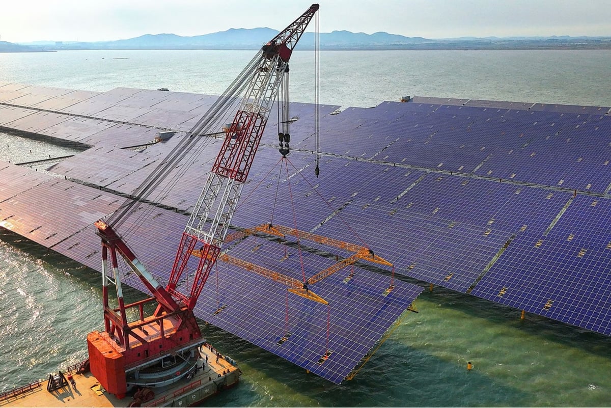 a crane lifts a huge solar panel into place on a lake