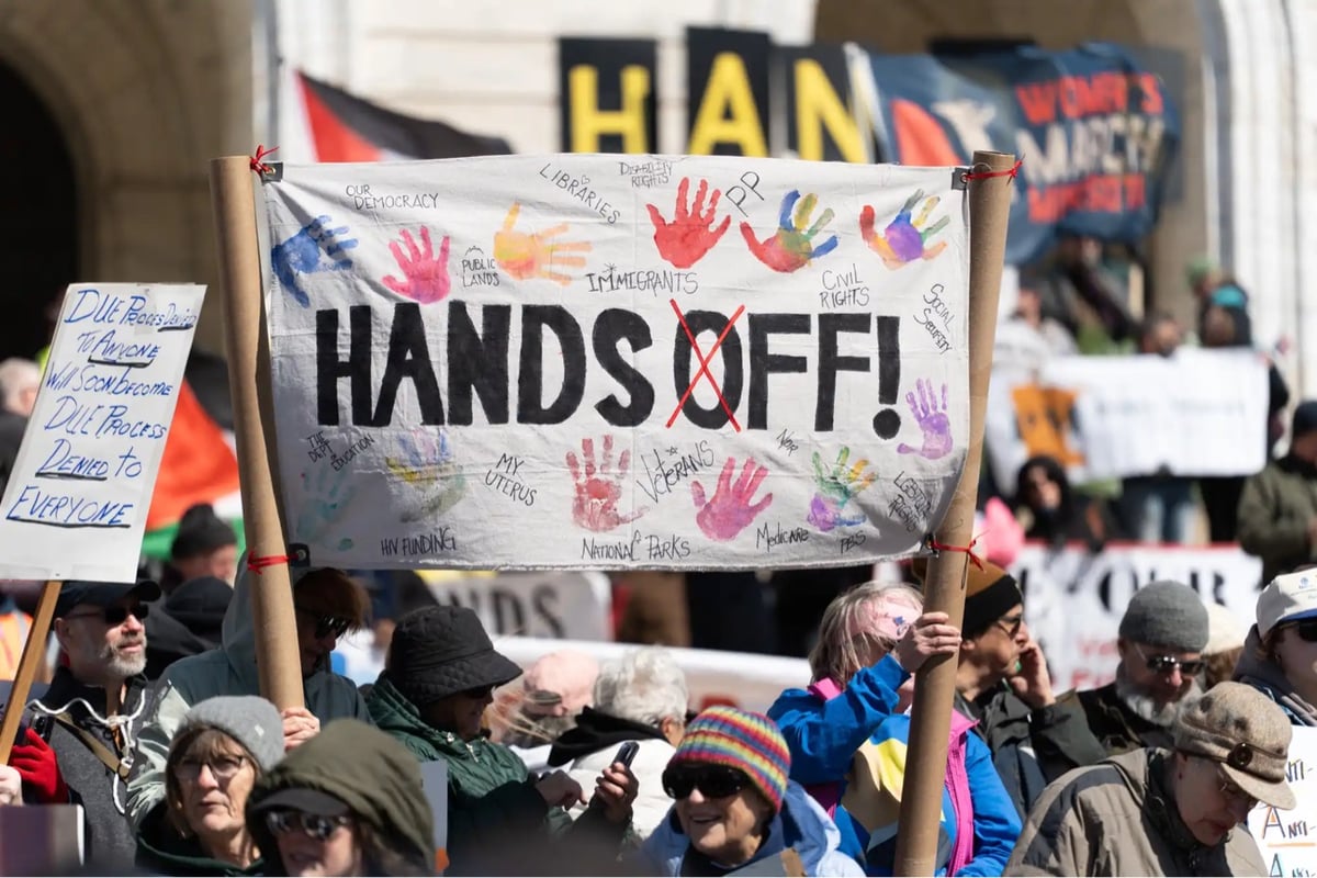 protesters hold signs, including a large 'Hands Off!' sign