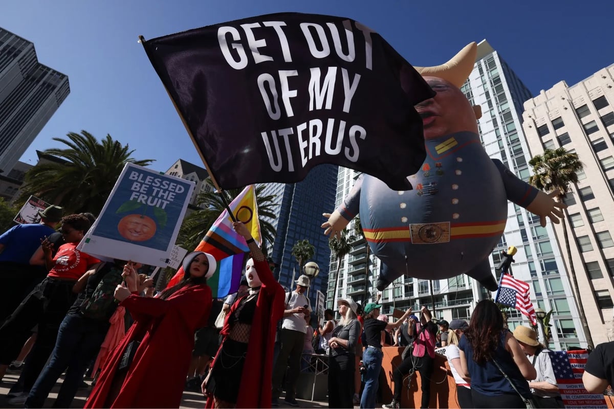 protesters hold signs, including a large 'get out of my uterus' sign