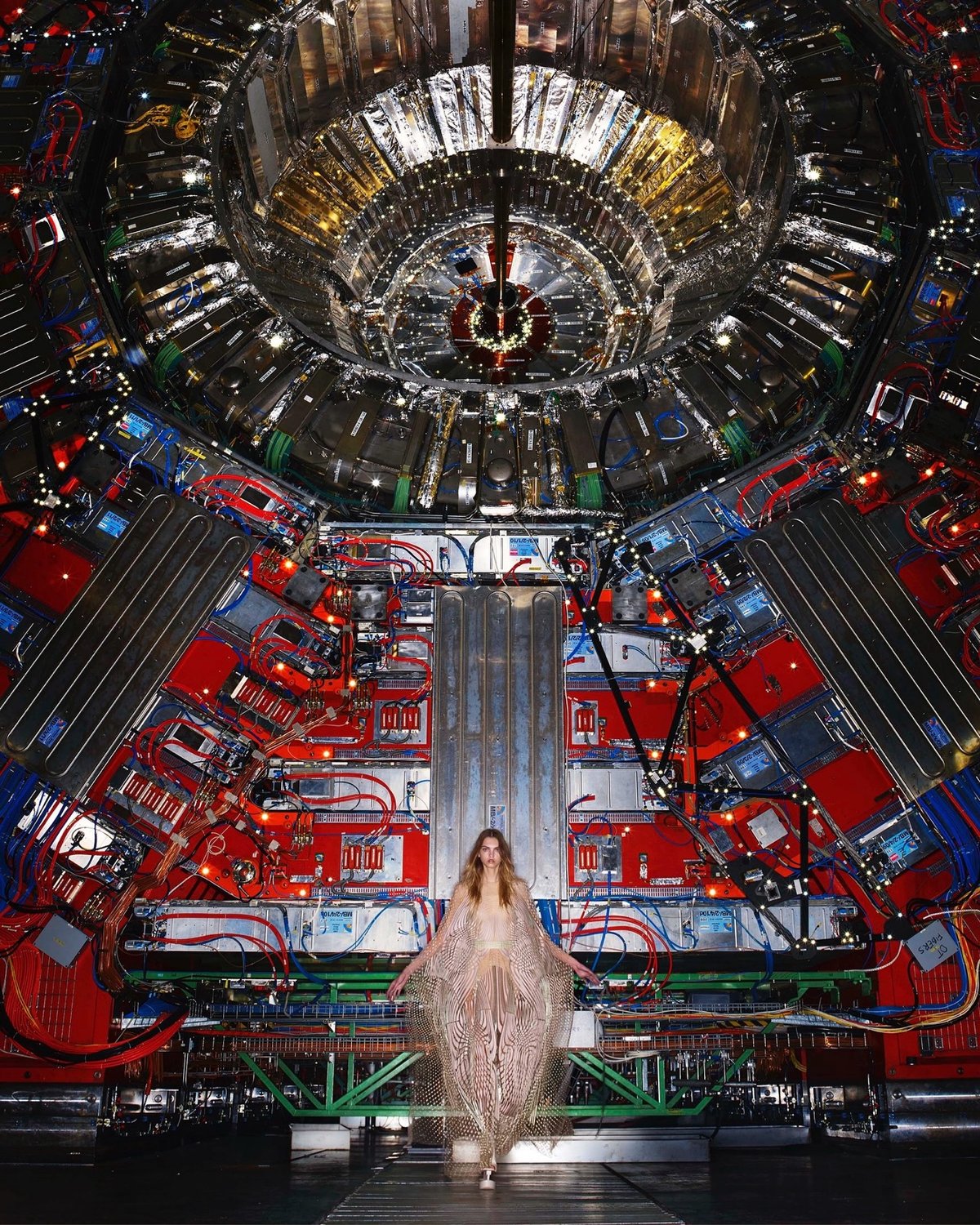 a model poses in front of a huge and very complicated scientific apparatus