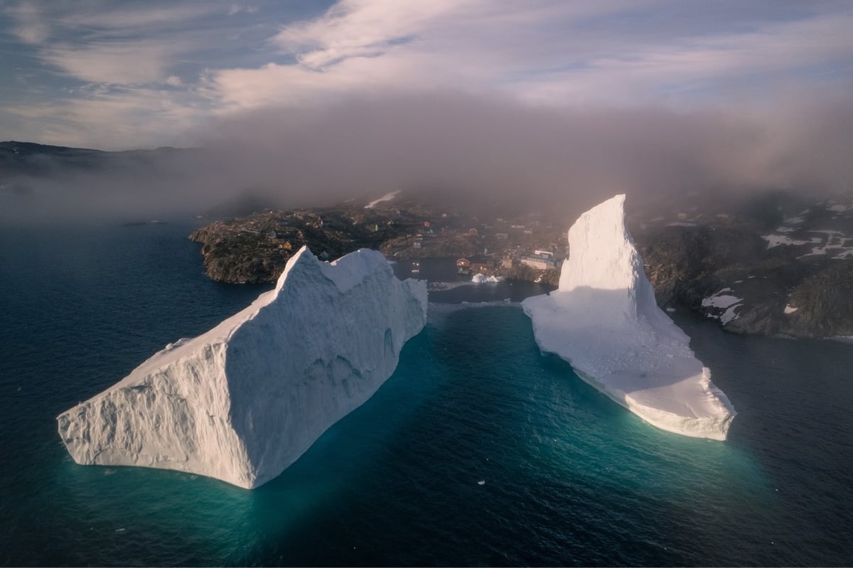 drone footage of two icebergs just off the coast of a small village