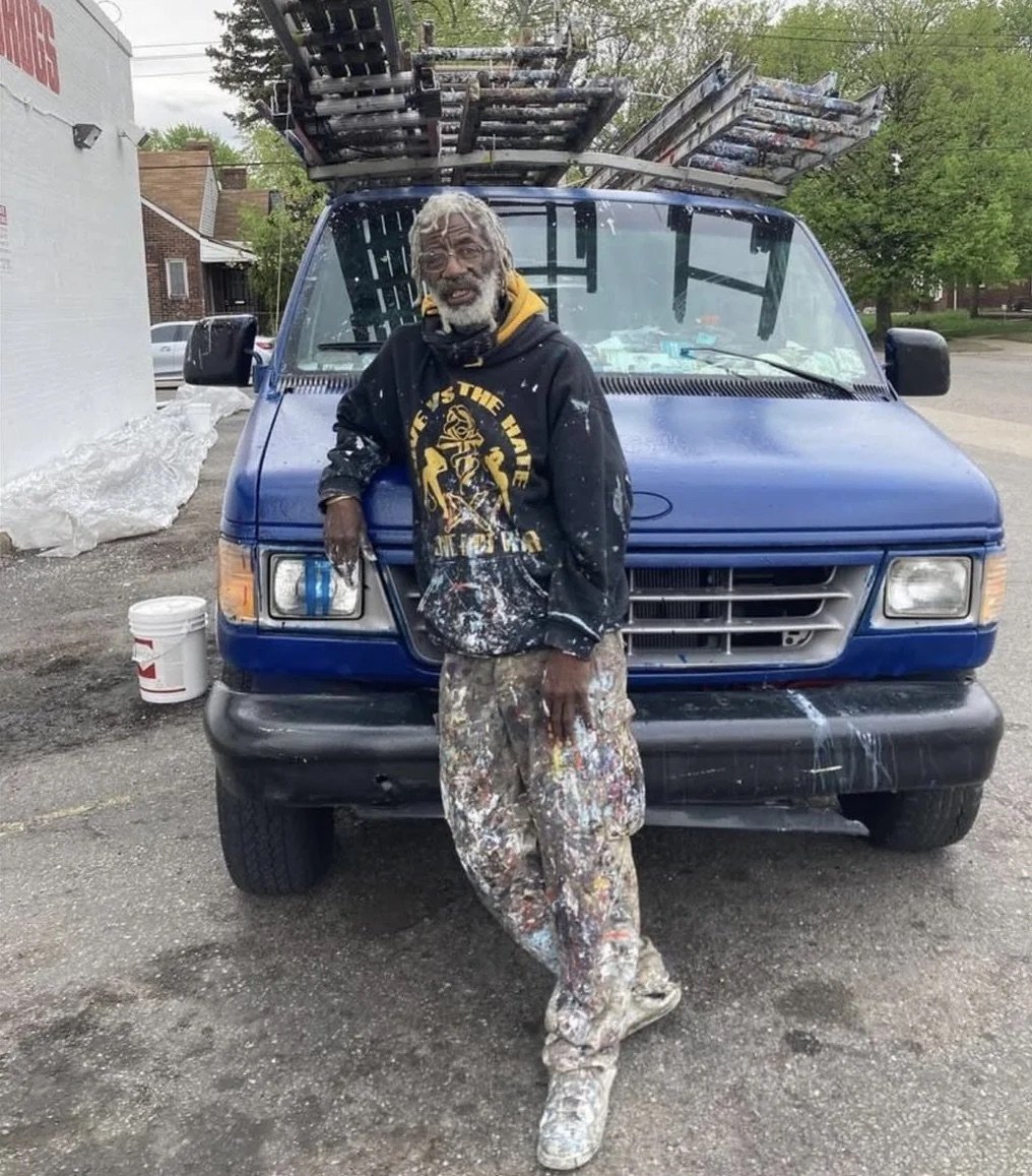 a photo of a man standing in front of a truck, covered in many different colors of paint