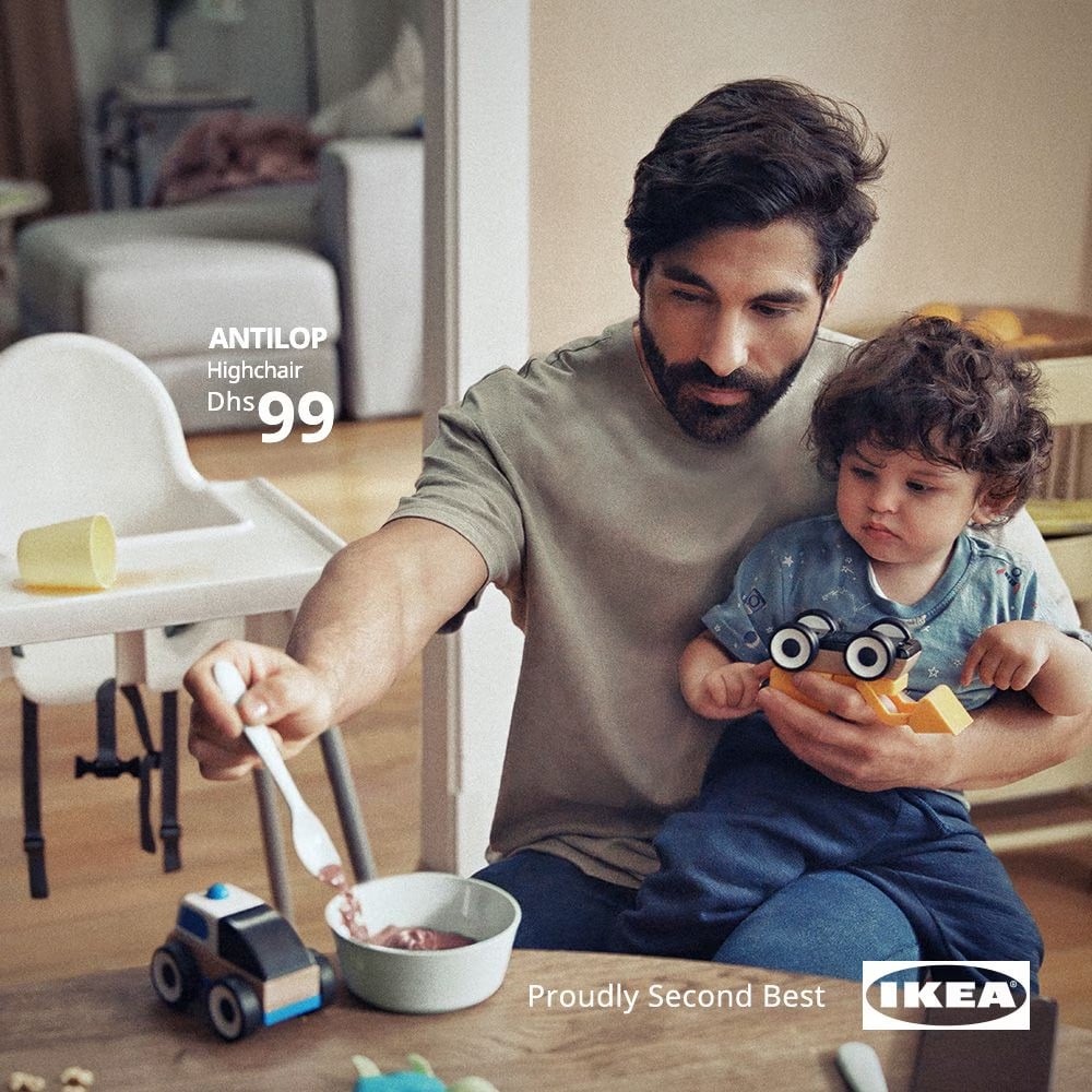 an Ikea ad with a kid eating on their father's knee instead of sitting in a nearby highchair