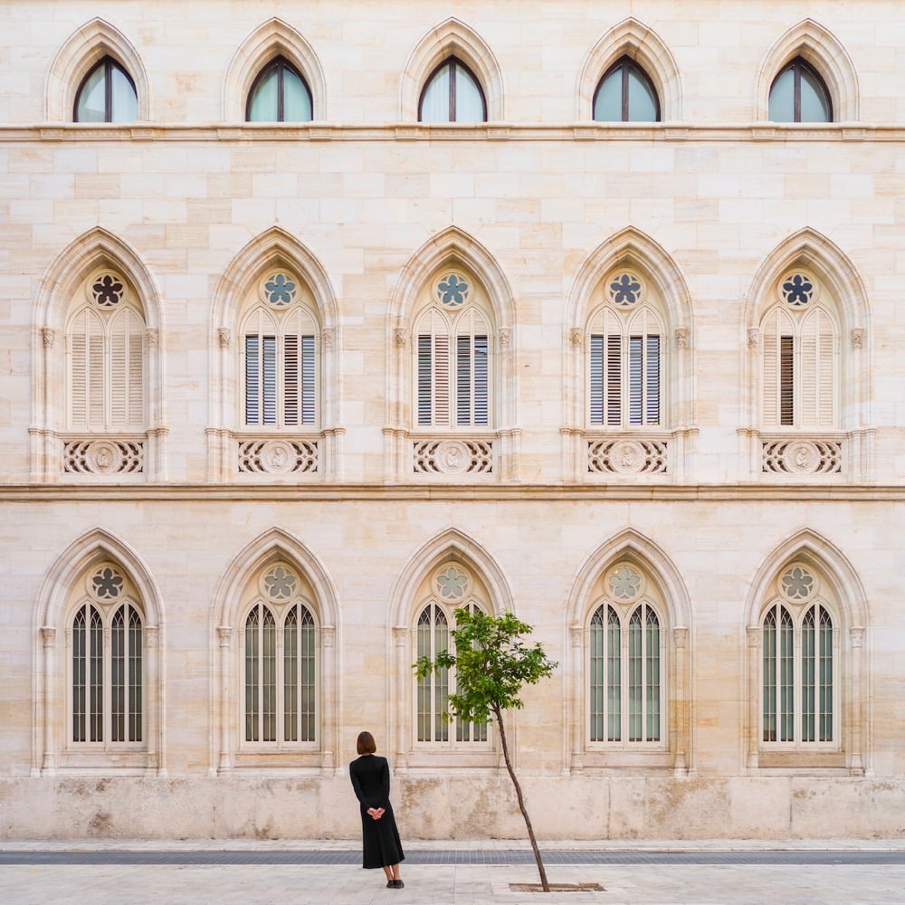 a woman and a tree lean the same way in front of a building