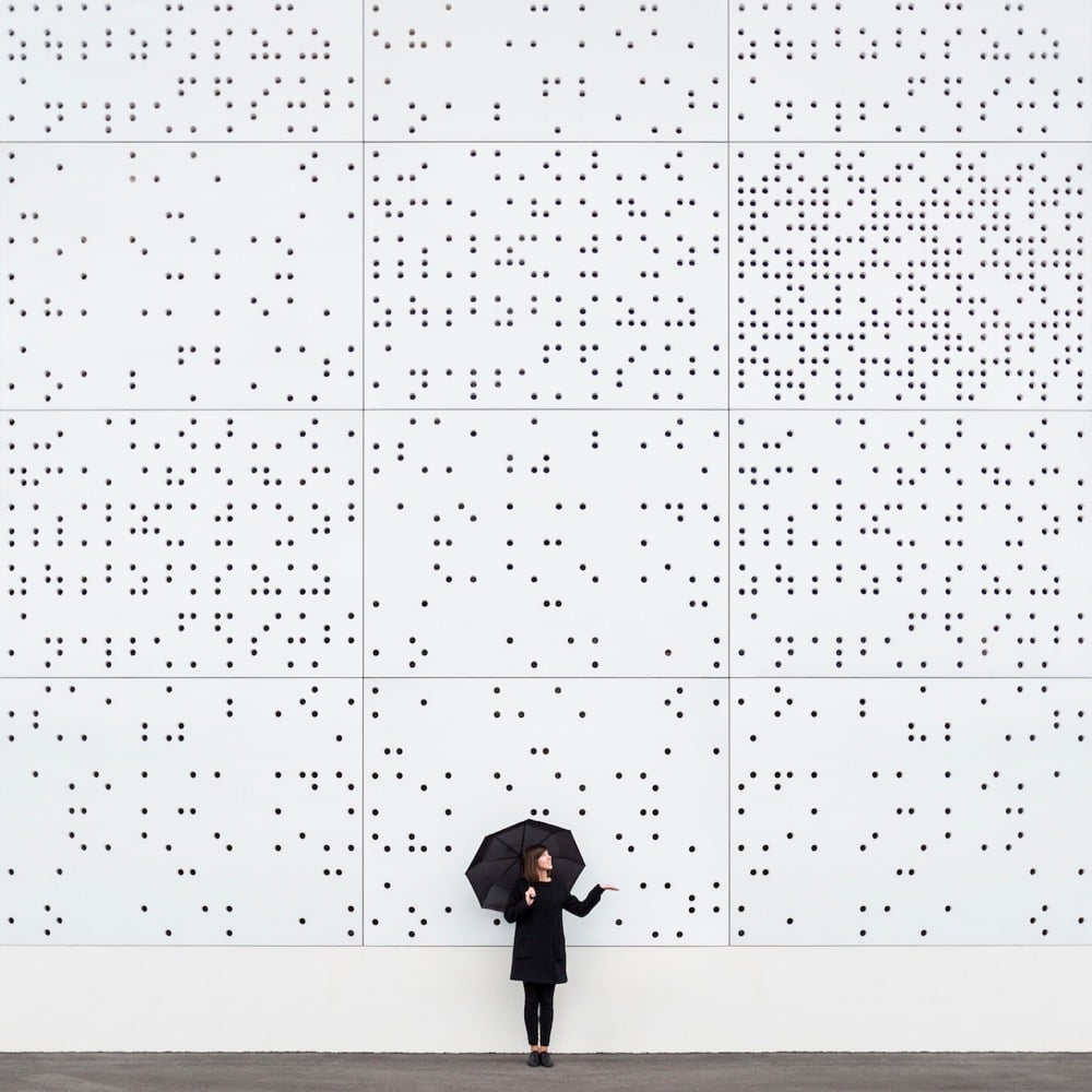 architectural dots on a wall appear to be raining down on a woman holding an umbrella