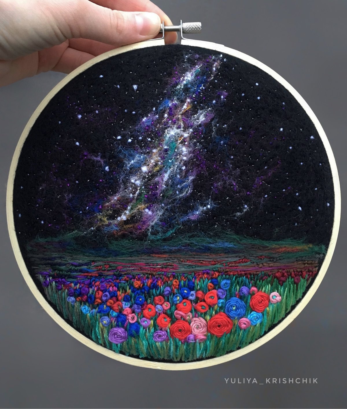 an embroidery piece of the Milky Way above a flowery meadow