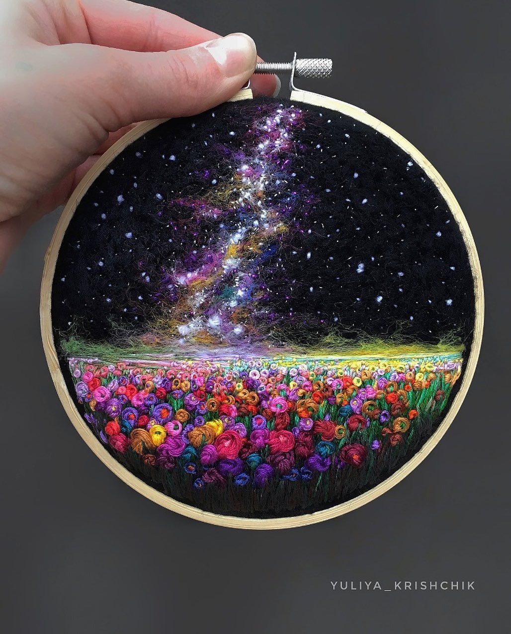 an embroidery piece of the Milky Way above a flowery meadow