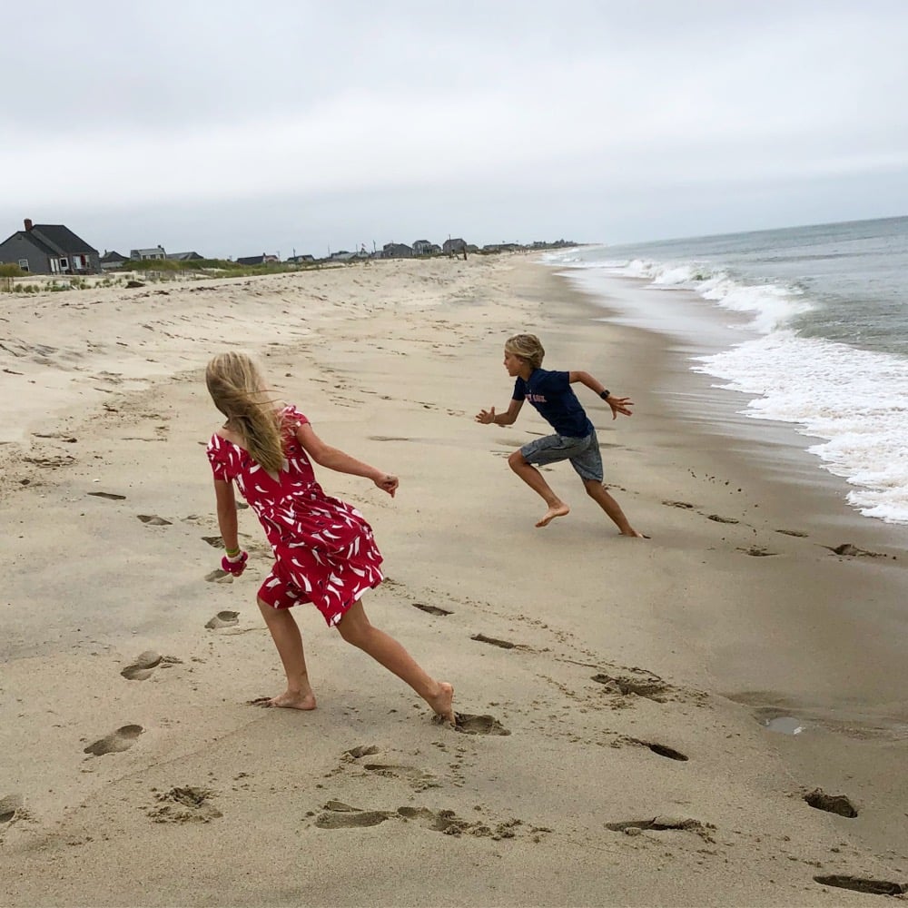two kids running from ocean waves on the beach