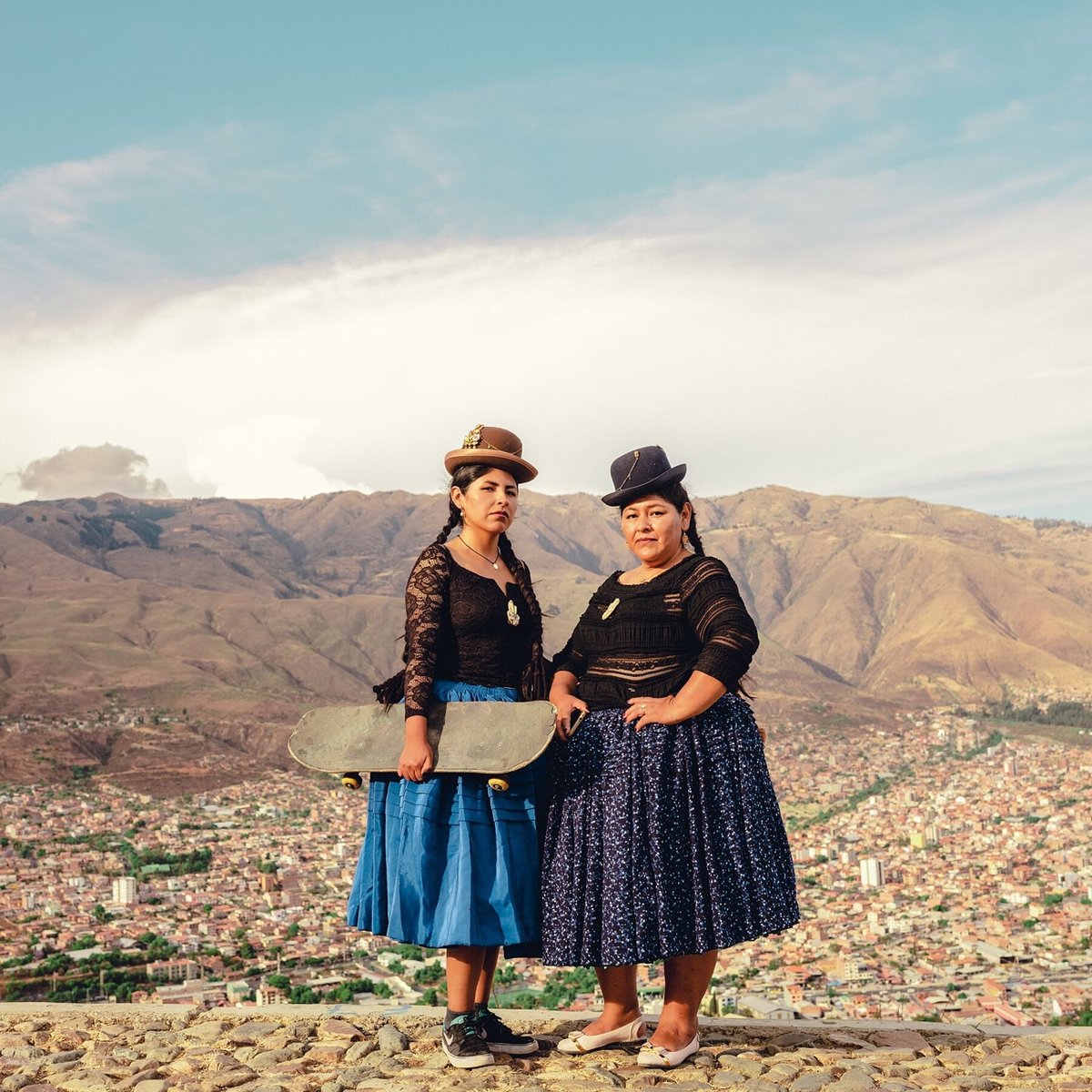 women in traditional Bolivian dress pose with a skatebaord