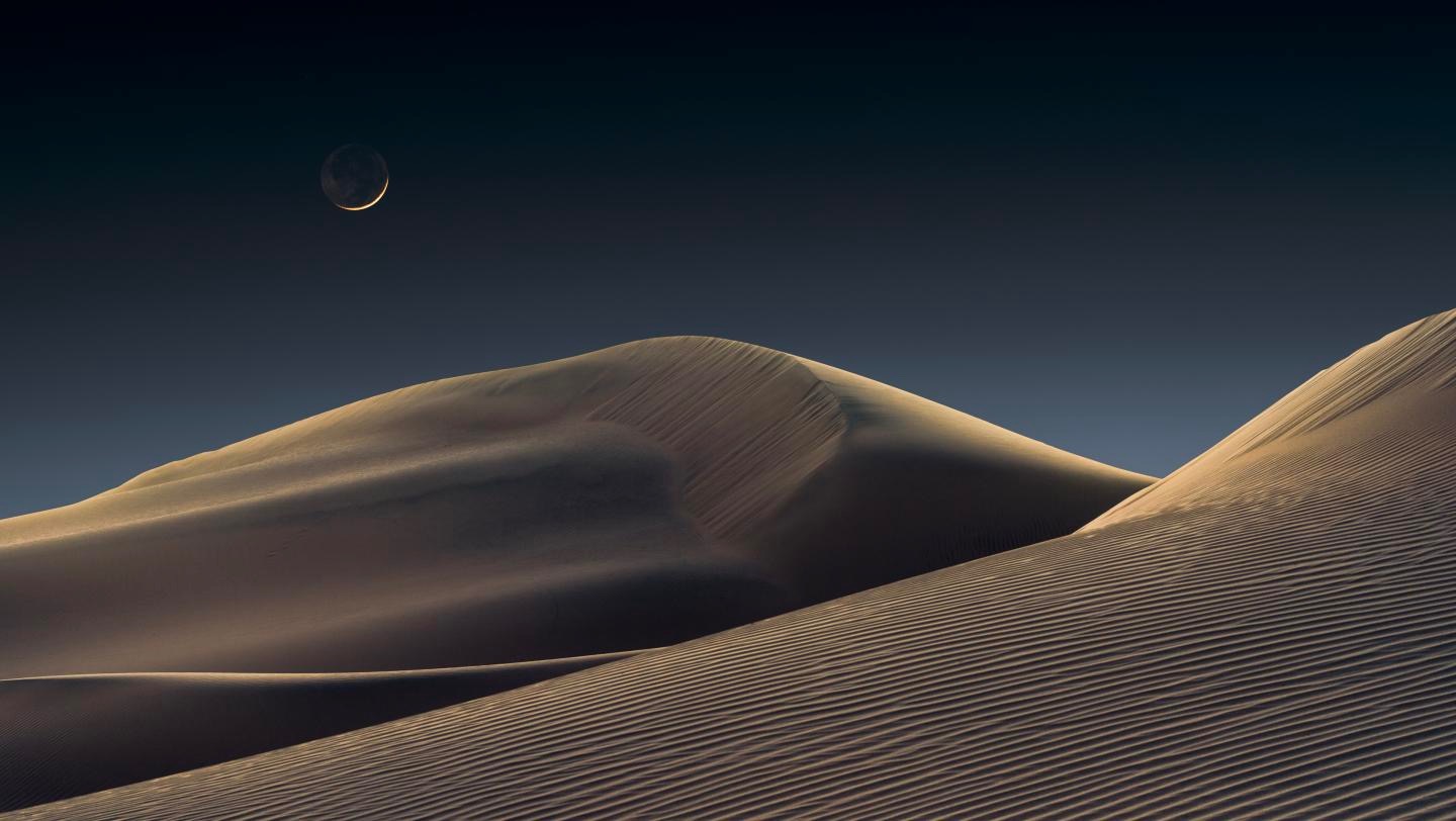 the crescent moon rising over the desert