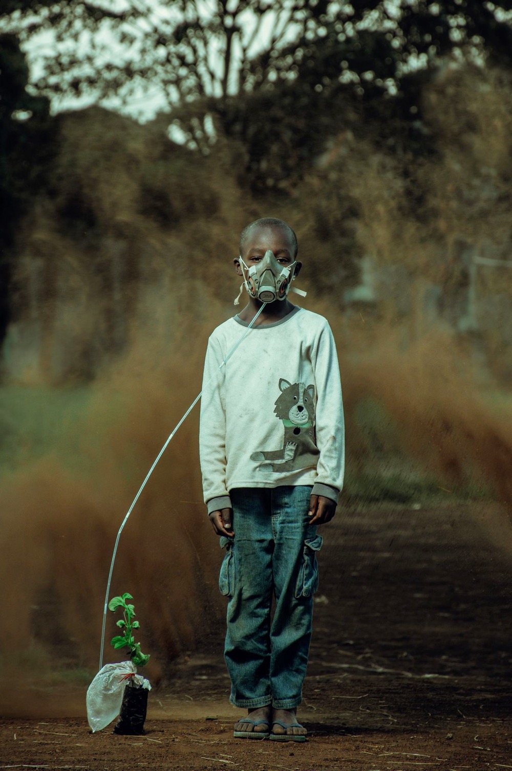 a boy wearing a gas mask connected to a potted plant