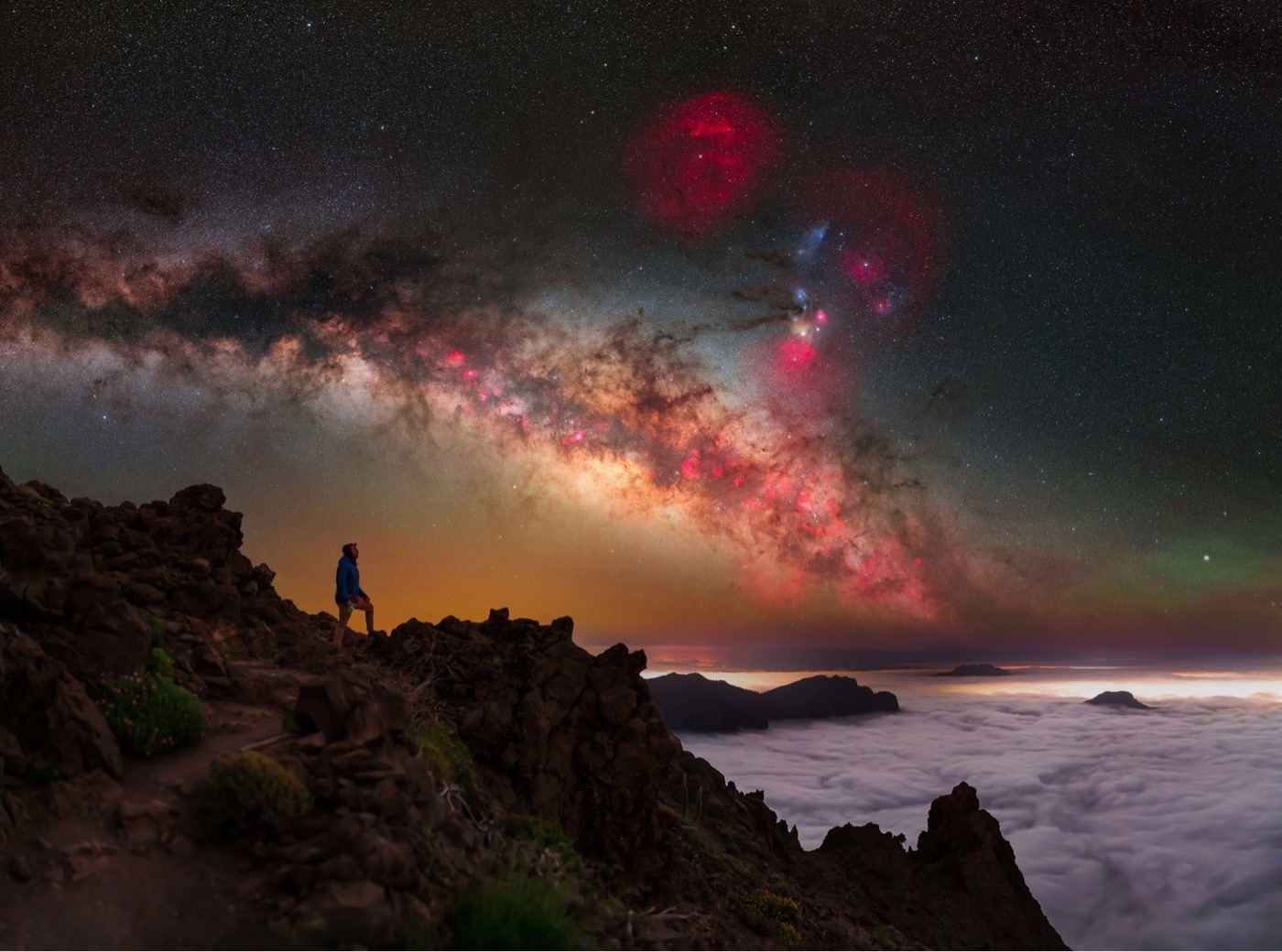 the Milky Way shines brilliantly at night above the mountains and a layer of clouds