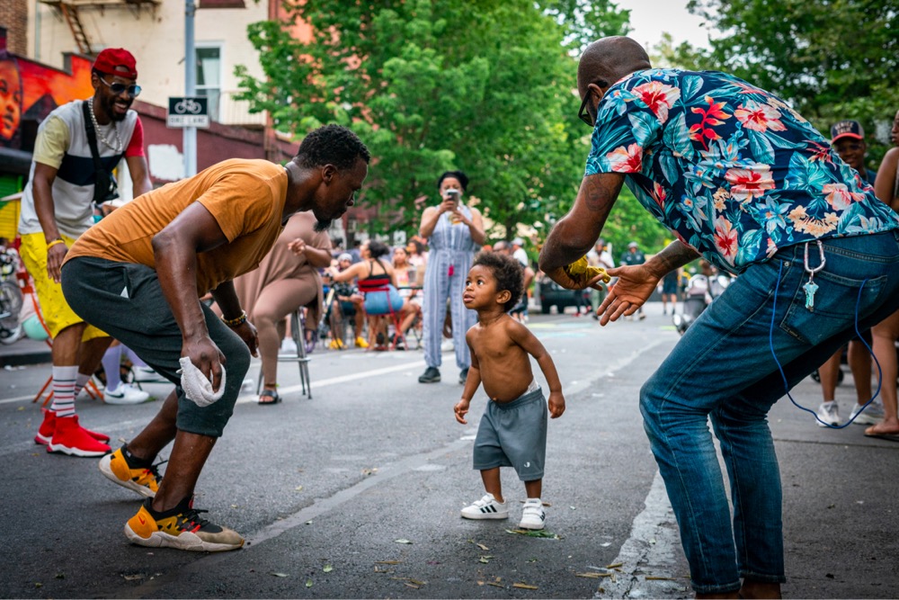 a small child dancing in the street surrounded by loving adults